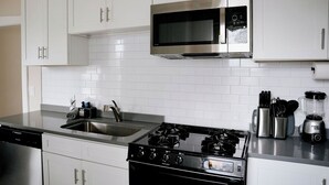 A modern kitchen with white cabinets, a stainless steel microwave, a gas stove, and a blender on the countertop. - Private Workspace •  Sleeps4 • Modern Stylish Stay (Chicago)