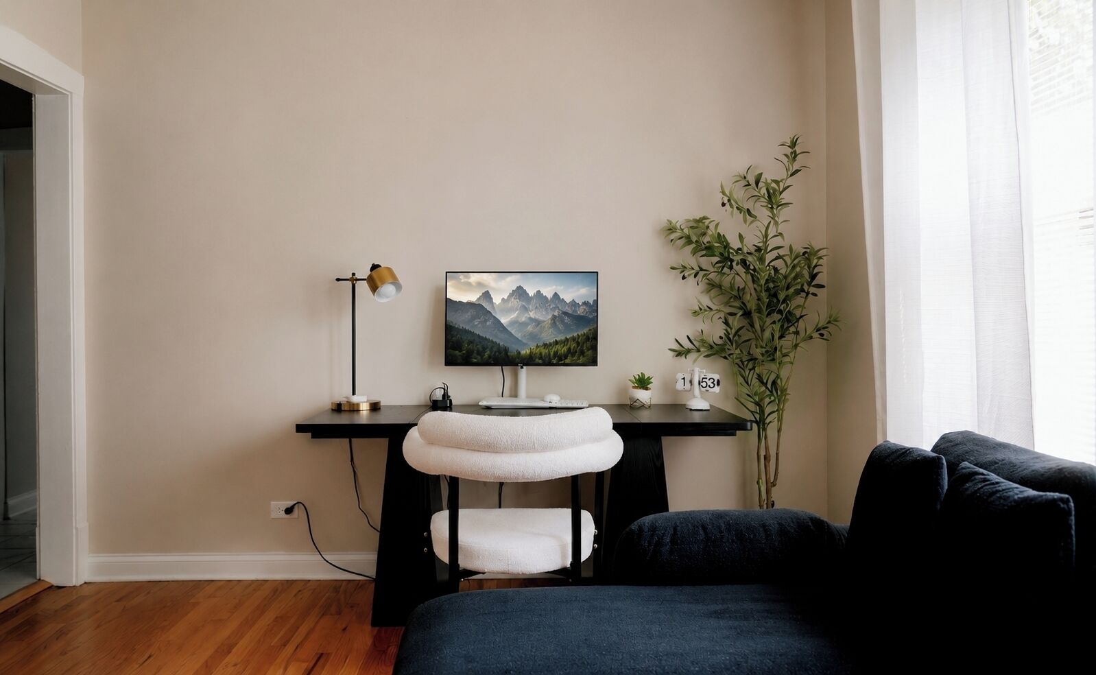 A room with a desk, a chair with a white cushion, a potted plant, and a large window.