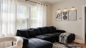A modern living room with a dark-colored sectional sofa, a white armchair, and a patterned rug.