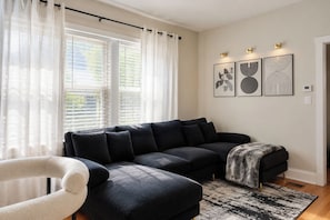 A modern living room with a dark-colored sectional sofa, a white armchair, and a patterned rug.
