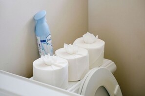 A toilet with a blue bottle of Febreze and three rolls of toilet paper with white floral decorations. - Private Workspace • Sleeps 4 • Modern and Stylish (Chicago)