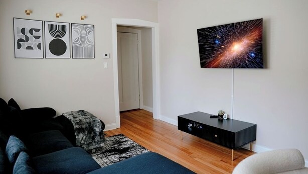 A modern living room with a sofa, a coffee table, and a flat-screen TV mounted on the wall. - Private Workspace •  Sleeps4 • Modern Stylish Stay (Chicago)