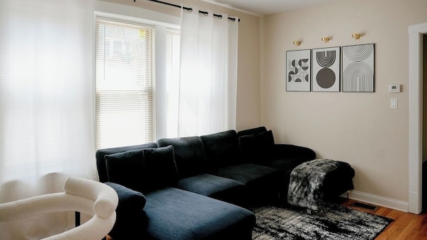 Ein Wohnzimmer mit einer Couch, einem weißen Sessel, einem Teppich mit Muster und Wandbildern.
