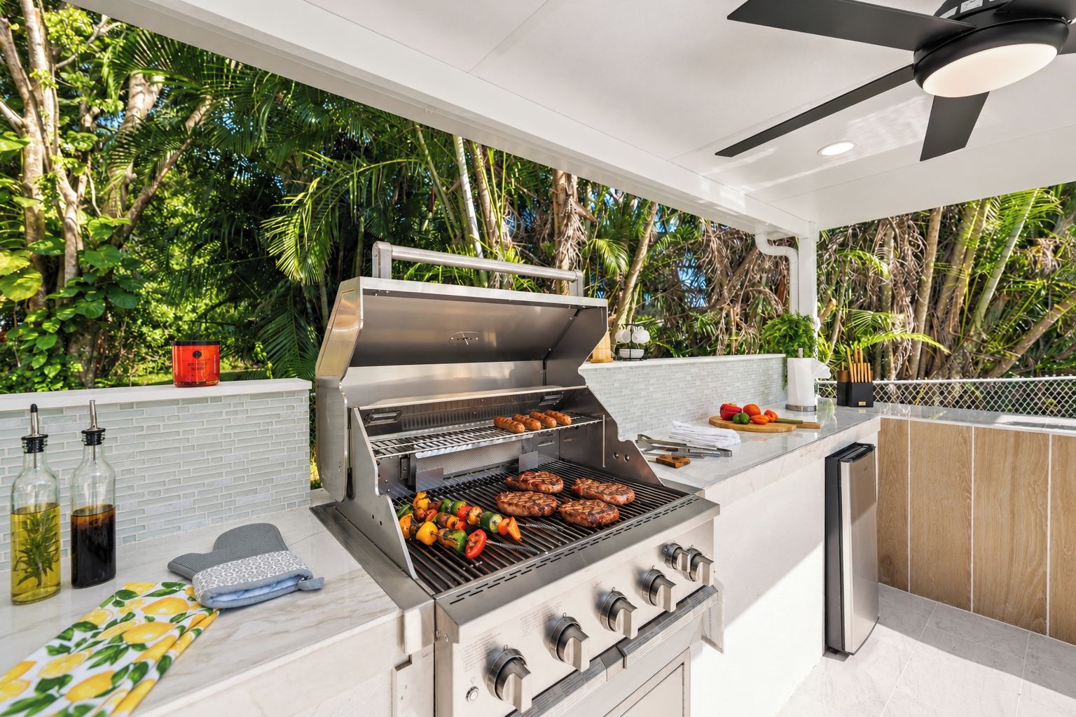 An outdoor kitchen with a grill, cooking utensils, and a view of lush greenery.