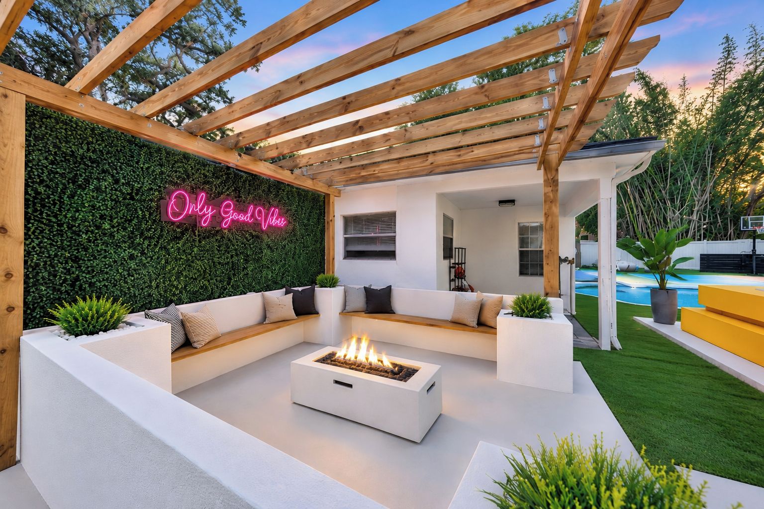 A modern outdoor patio with a built-in fire pit, white sofas, and a neon sign.