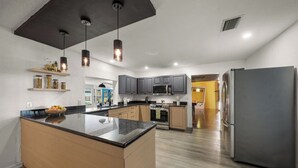 Una cocina moderna con una isla central, electrodomésticos integrados e iluminación colgante.