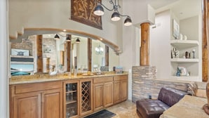 A spacious kitchen with a curved island, wooden cabinets, and a stone accent wall. - Sleeps 25 • Heated Pool and Spa • Pickleball Court (Scottsdale)