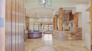 A spacious living area with a stone fireplace, a large sectional sofa, and a dining area with a kitchen in the background. - Sleeps 25 • Heated Pool and Spa • Pickleball Court (Scottsdale)