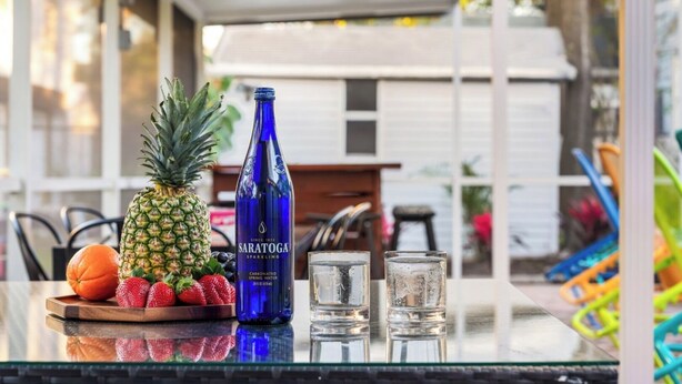 A table with a bottle of Saratoga sparkling water, a pineapple, strawberries, an orange, and two glasses. - Sleeps 25 • Heated Pool• In+Outdoor Games •Theater (Tampa)