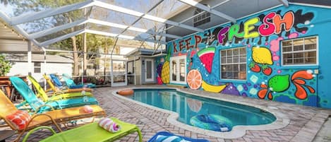A pool area with colorful lounge chairs and a mural on the wall.
