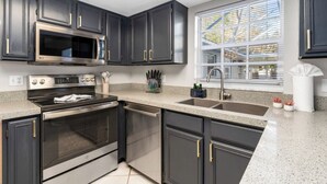 A modern kitchen with dark cabinets, stainless steel appliances, a granite countertop, and a window with blinds. - Sleeps 25 • Heated Pool• In+Outdoor Games •Theater (Tampa)
