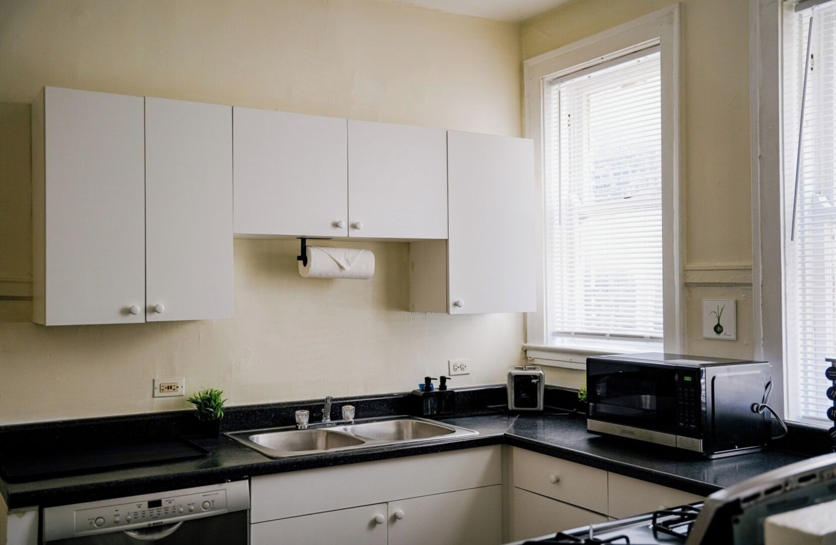 A kitchen with white cabinets, a black countertop, a stainless steel sink, a toaster, and a microwave.