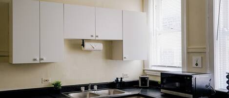 A kitchen with white cabinets, a black countertop, a stainless steel sink, a toaster, and a microwave.
