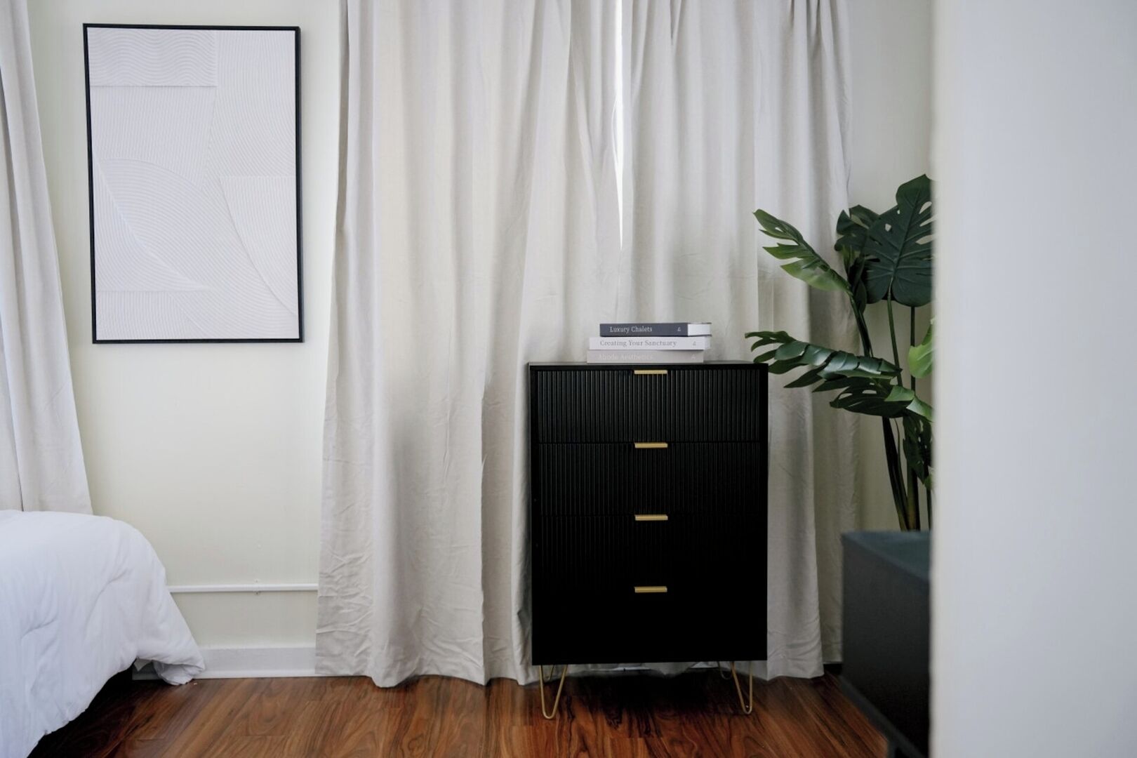 A bedroom with a bed, a black cabinet with books, and a plant.
