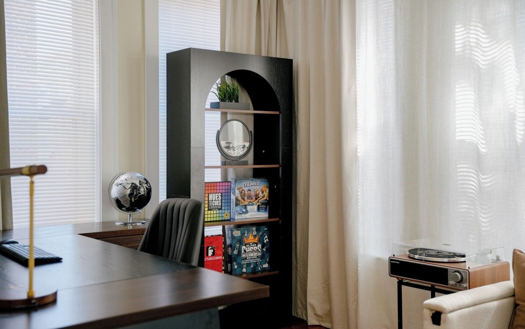 A room with a desk, a globe, a bookshelf with board games, and a small table with a radio.