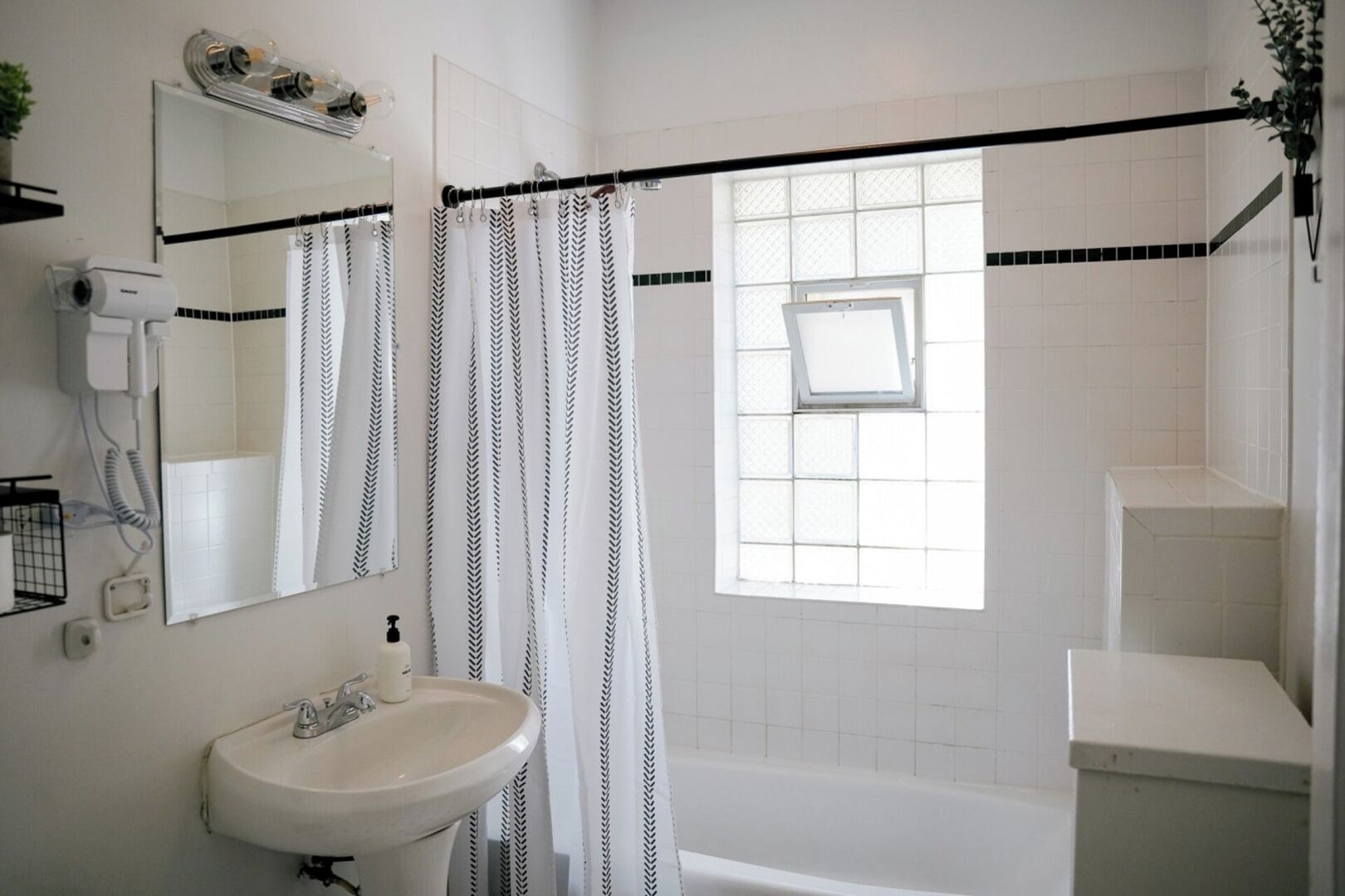 A bathroom with a white sink, a mirror, a shower curtain, a window, and a bathtub.