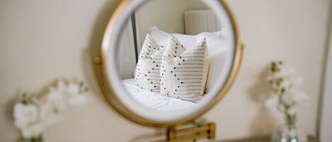 A round mirror with a gold frame on a dresser, reflecting a bed with striped pillows.