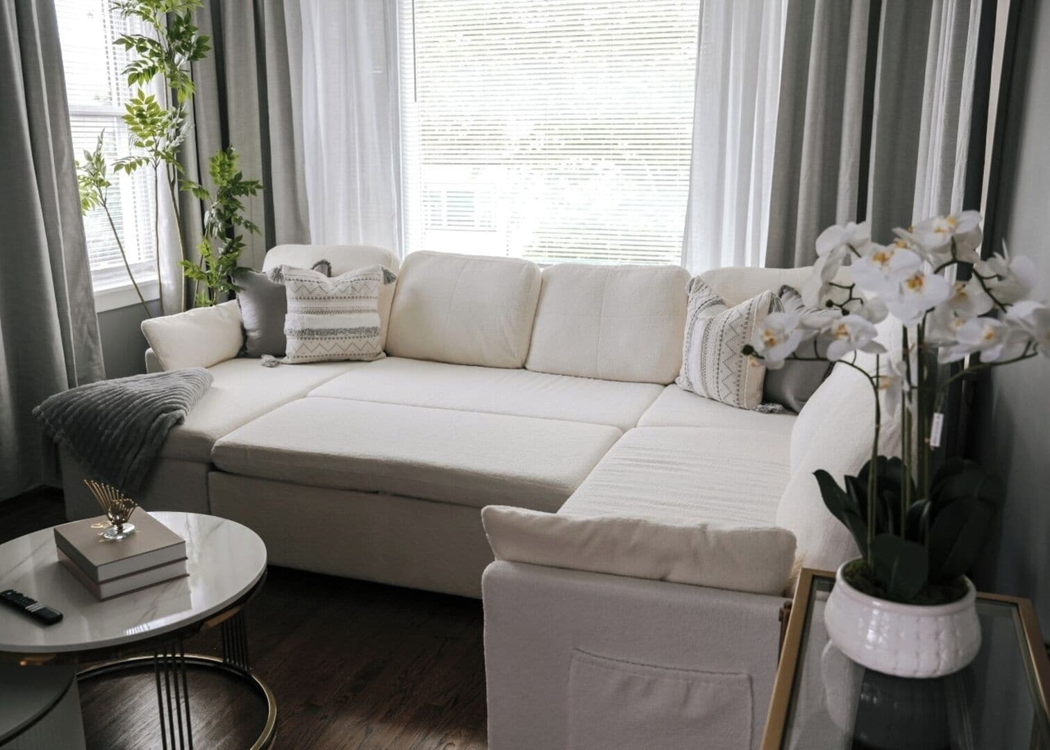 Una sala de estar moderna con un sofá seccional color beige, una mesa de centro redonda y una orquídea en maceta.