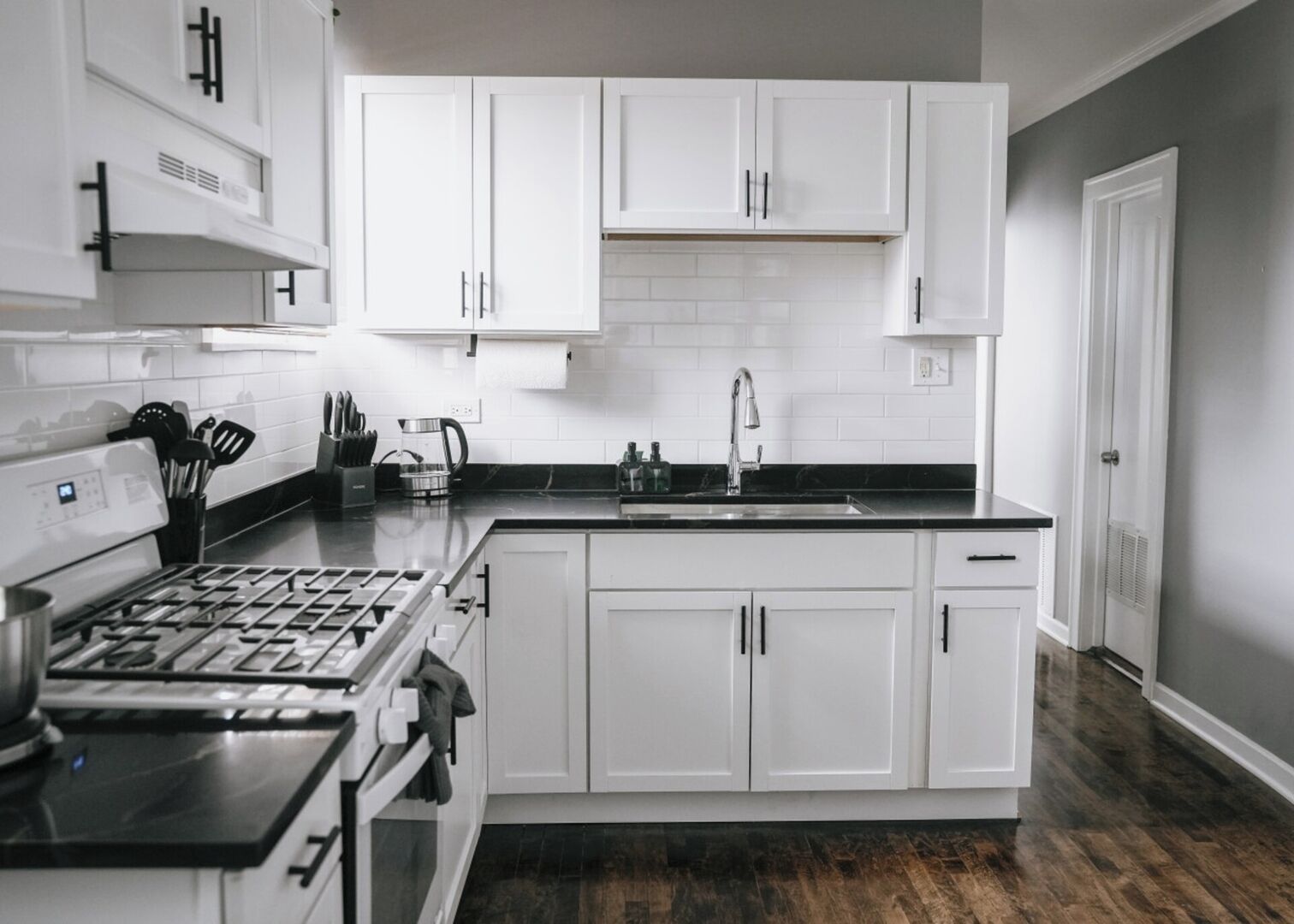 A modern kitchen with white cabinetry, a stainless steel stove, and a black countertop.
