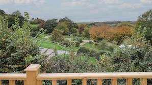 A view from a wooden deck overlooking a landscaped garden with a pathway, trees, and a distant view of hills. - Avalon (Lyme Regis)