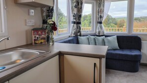 A compact kitchen with a sink, a small cabinet, and a window with curtains. - Avalon (Lyme Regis)