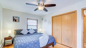 Une chambre à coucher avec un lit, un plancher en bois, un ventilateur de plafond, une fenêtre et une armoire.