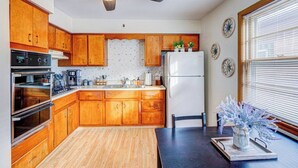 Une cuisine avec des meubles de rangement en bois, une cuisinière, un four, un réfrigérateur et un ventilateur de plafond.