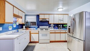 A modern kitchen with white cabinets, a stainless steel refrigerator, a gas stove, and a coffee bar sign. - King Bed Studio | 60" HDTV | Safe | Close to Metra (Elmwood Park)