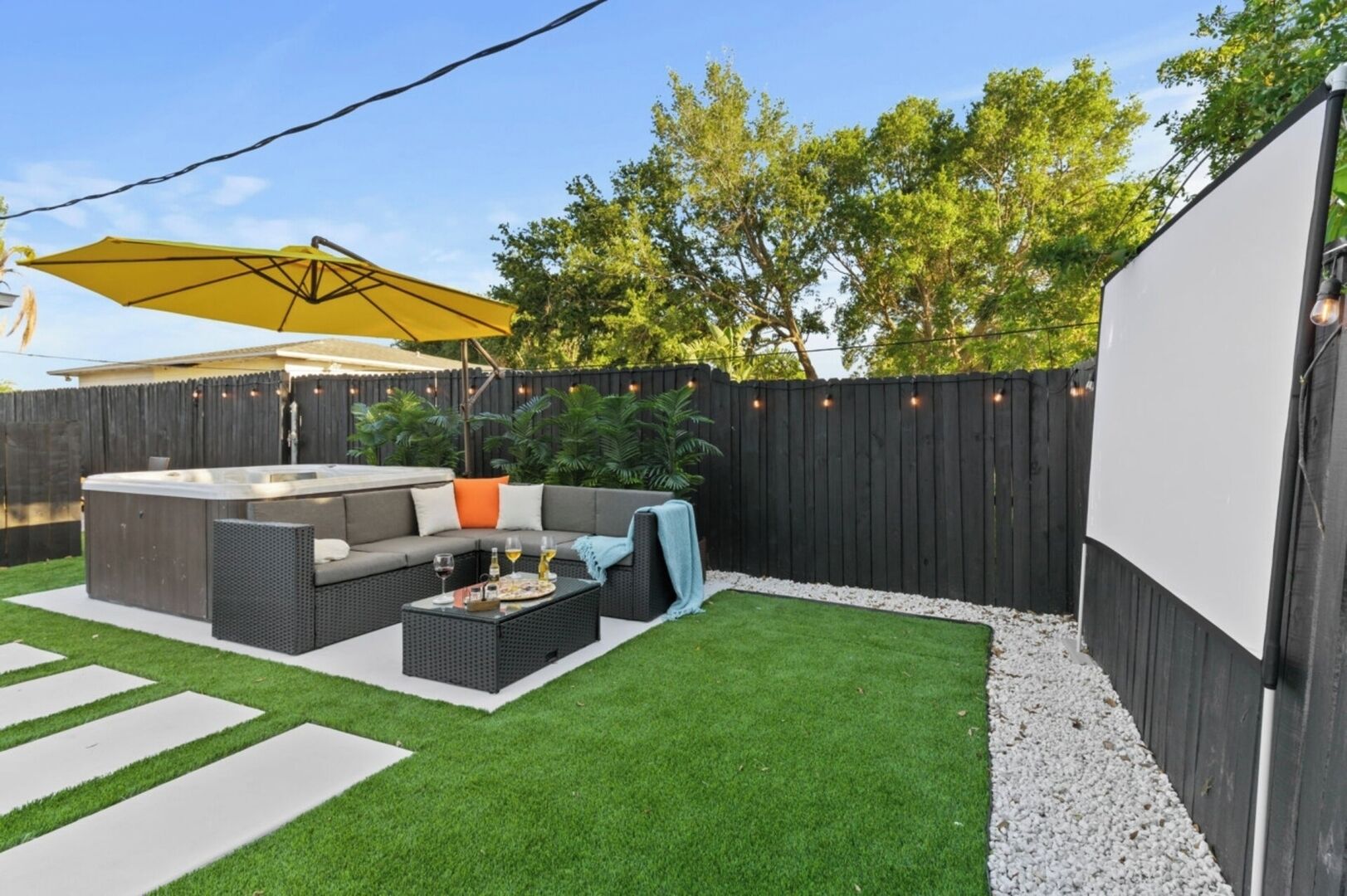 A backyard with a hot tub, outdoor seating, and a pergola with string lights.