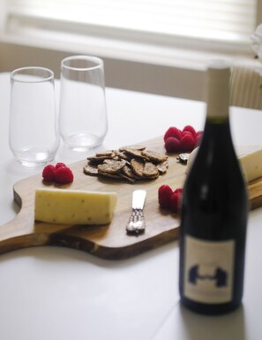 A wooden board with cheese, crackers, and raspberries on a table. Two glasses and a bottle of wine are also visible. - Private Workspace • Sleeps 4 New Modern 1BR • (Chicago)