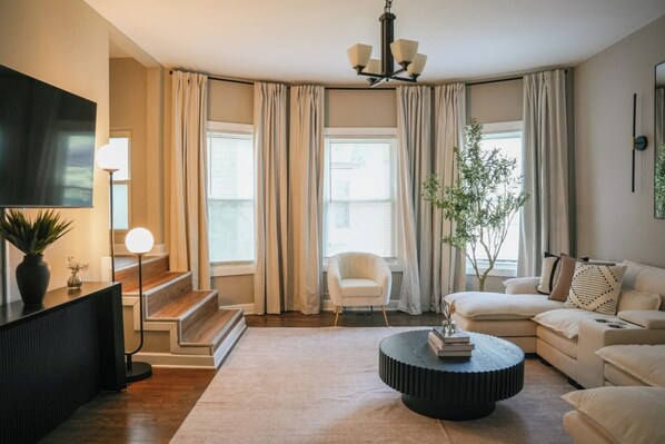 A modern living room with a sofa, coffee table, TV, and a staircase.