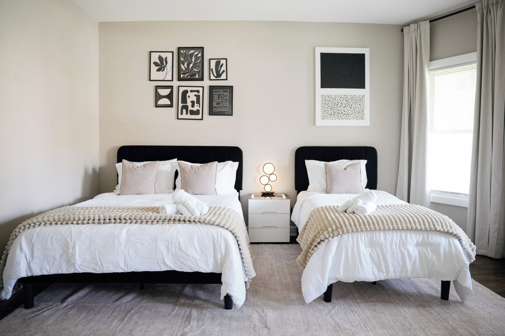 A double bed room with a large window, a bedside table, and a wall with framed artwork.