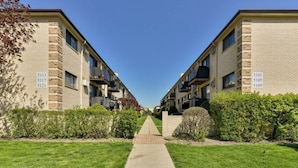 A row of brick apartment buildings with numbered doors, a clear sky, and a well-maintained lawn.