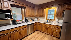 A kitchen with wooden cabinets, a stainless steel refrigerator, a microwave, a dishwasher, and a window with a view of the outdoors. - Quaint Small Town Home - Country Style Living in Independence (Independence)