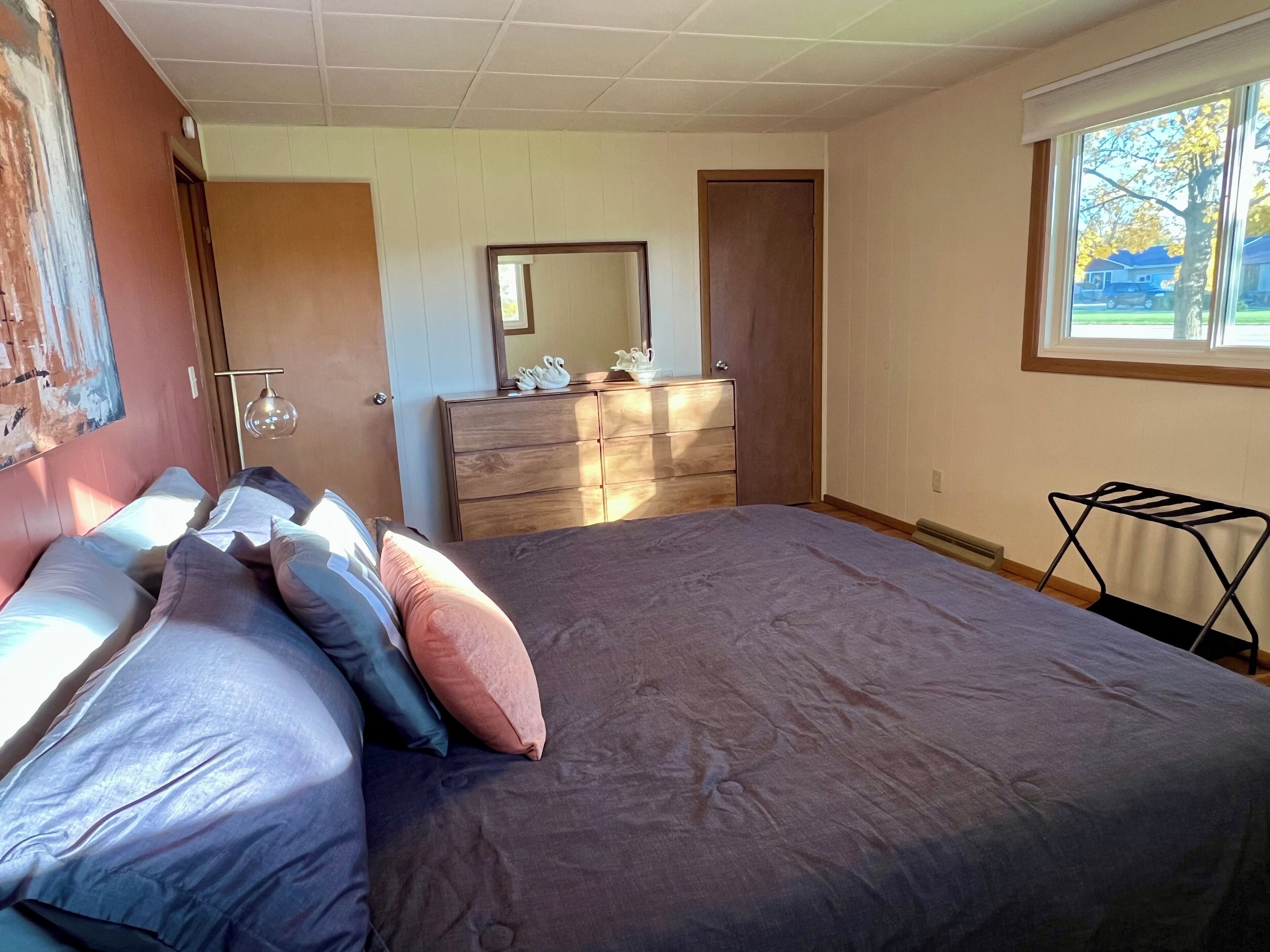 Un dormitorio con cama, cómoda, espejo y ventana.