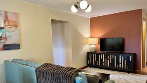 A living room with a blue sofa, a black entertainment unit, a flat-screen TV, and a painting on the wall. - Quaint Small Town Home - Country Style Living in Independence (Independence)