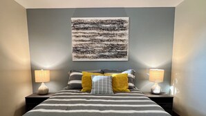 A neatly made bed with striped bedding, two bedside lamps, and a large abstract painting on the wall. - Quaint Small Town Home - Country Style Living in Independence (Independence)