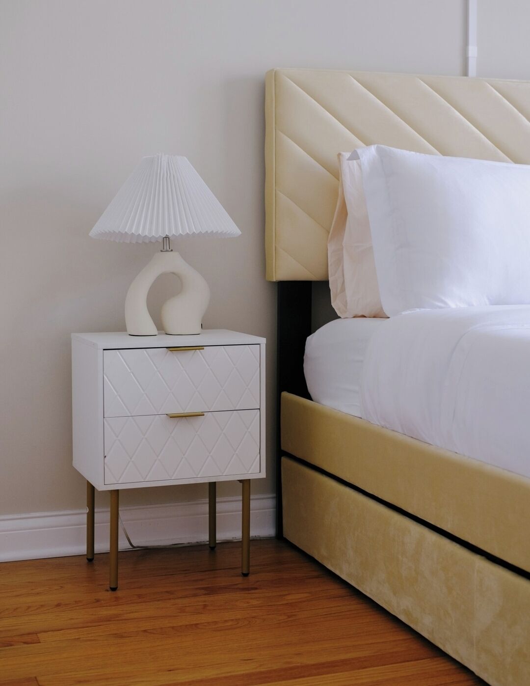 A neatly arranged bedroom with a bed, a bedside table with a lamp, and a small white cabinet.