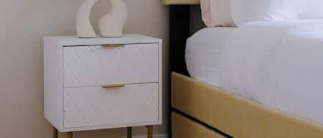 A neatly arranged bedroom with a bed, a bedside table with a lamp, and a small white cabinet.