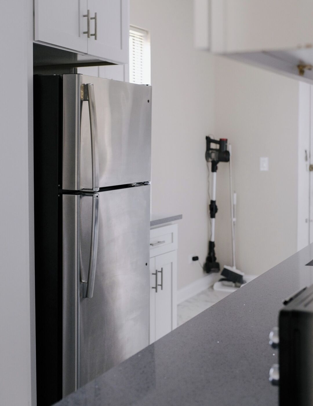 A kitchen with a stainless steel refrigerator, white cabinets, and a black countertop.