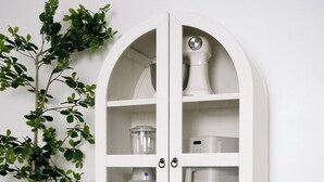 Un meuble blanc à arc, doté de portes en verre, contenant des appareils de cuisine tels qu’un mixeur, un grille-pain et une bouilloire.