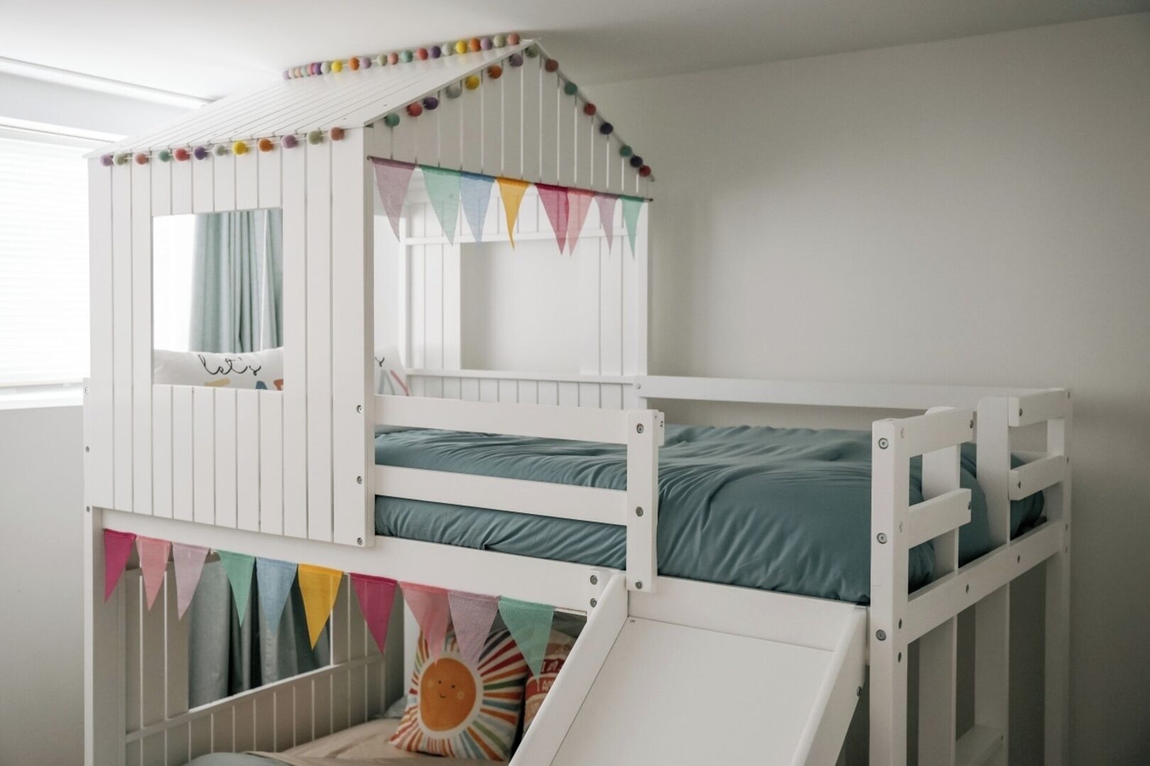 Ein Stockbett mit einer kleinen Rutsche, weißen Wänden und farbenfroher Girlande.