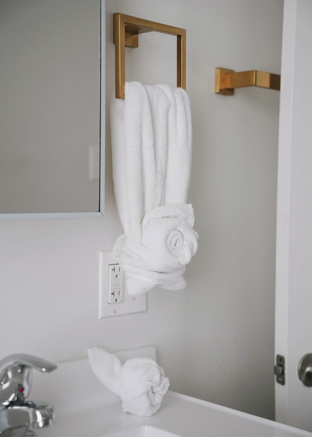 Une salle de bain avec un lavabo blanc, un miroir et un porte-serviettes avec deux serviettes.