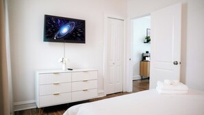 Une chambre à coucher comprenant un lit, une commode, un téléviseur fixé au mur et une porte donnant sur une salle de bain.