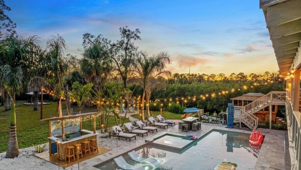 A pool area with lounge chairs, a bar, and a staircase leading to a deck. - Sleeps 40! 13BR•Heated Pool•Waterfront Resort•Spa (Tampa)