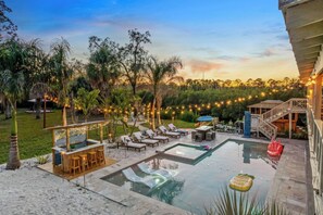 Zona de piscina con sillones de descanso, un bar y una escalera que lleva a una terraza.