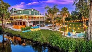 A large green building with a covered patio area, a pool, and a waterfront view. - Sleeps 40! 13BR•Heated Pool•Waterfront Resort•Spa (Tampa)