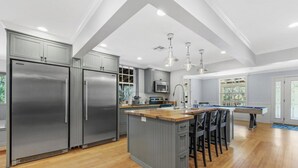 A modern kitchen with grey cabinetry, stainless steel appliances, a wooden island with bar stools, and a pool table. - Sleeps 40! 13BR•Heated Pool•Waterfront Resort•Spa (Tampa)