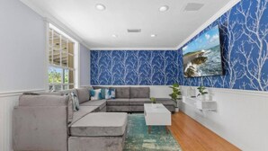 A living room with a grey sectional sofa, a white coffee table, and a blue patterned wall. - Sleeps 40! 13BR•Heated Pool•Waterfront Resort•Spa (Tampa)