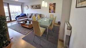 A modern living room with a glass dining table, beige sofa, and a large window. - Apartamentos Pilartxo Jaca 3000 (Jaca)
